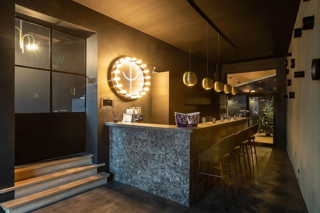 Moderne bar met mozaïektoog, hanglampen en sfeerverlichting in donkere ruimte met kerstboom op achtergrond.