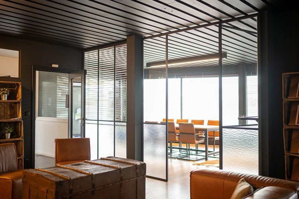 Moderne vergaderruimte met glazen wanden, houten tafel en leren stoelen in een industrieel interieur.