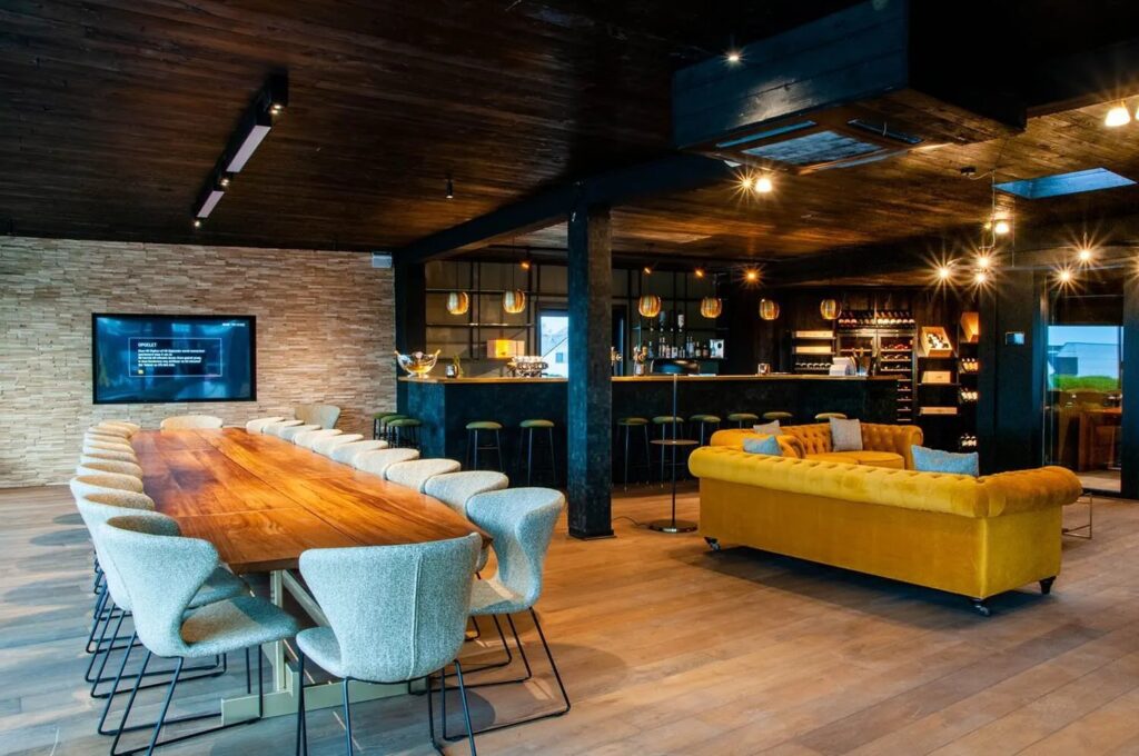 Moderne vergaderruimte met lange houten tafel, gele bank en stijlvolle bar met verlichting.
